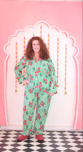 Load image into Gallery viewer, Woman in a green pajama set with red cherries on a pink background.