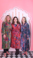 Load image into Gallery viewer, Three women wearing colorful patterned robes standing in front of a decorative pink wall.